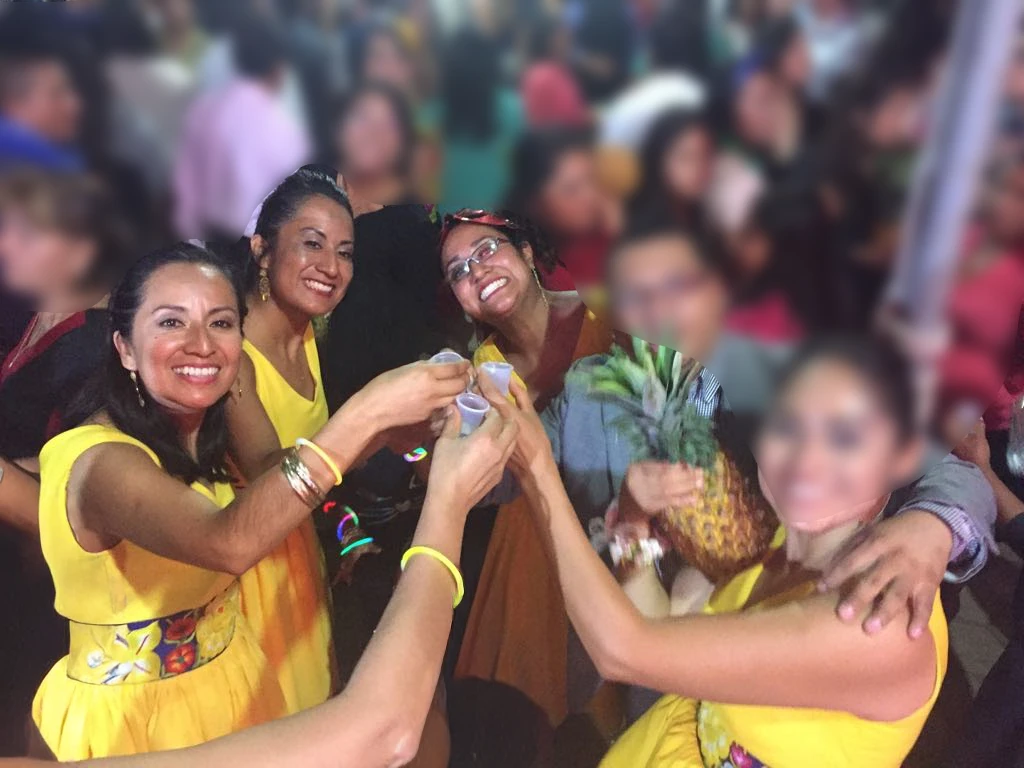 Group toasting with jícaras during a traditional celebration, wearing bright yellow outfits.