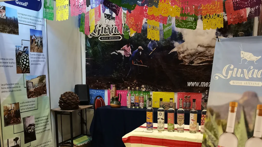 Guxadi Mezcal Artesanal booth with papel picado and traditional process display.
