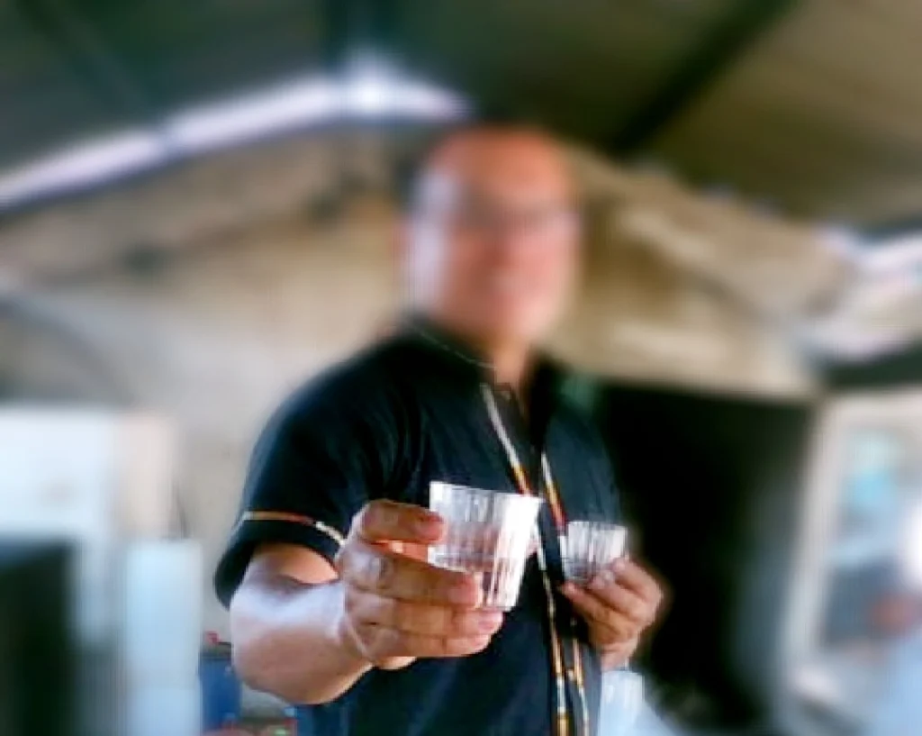 Homme offrant un verre de mezcal avec un geste de partage.